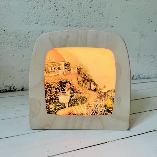 Wooden lamp with a printed design of a couple in a garden on a white surface.