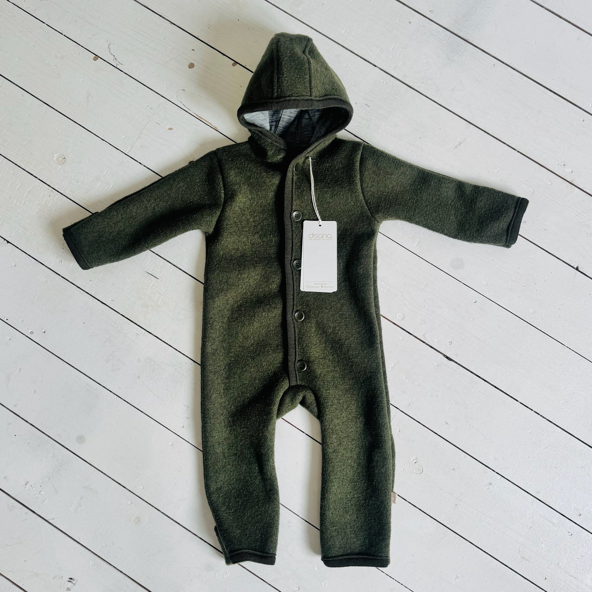 Green baby onesie with a hood on a light wooden floor