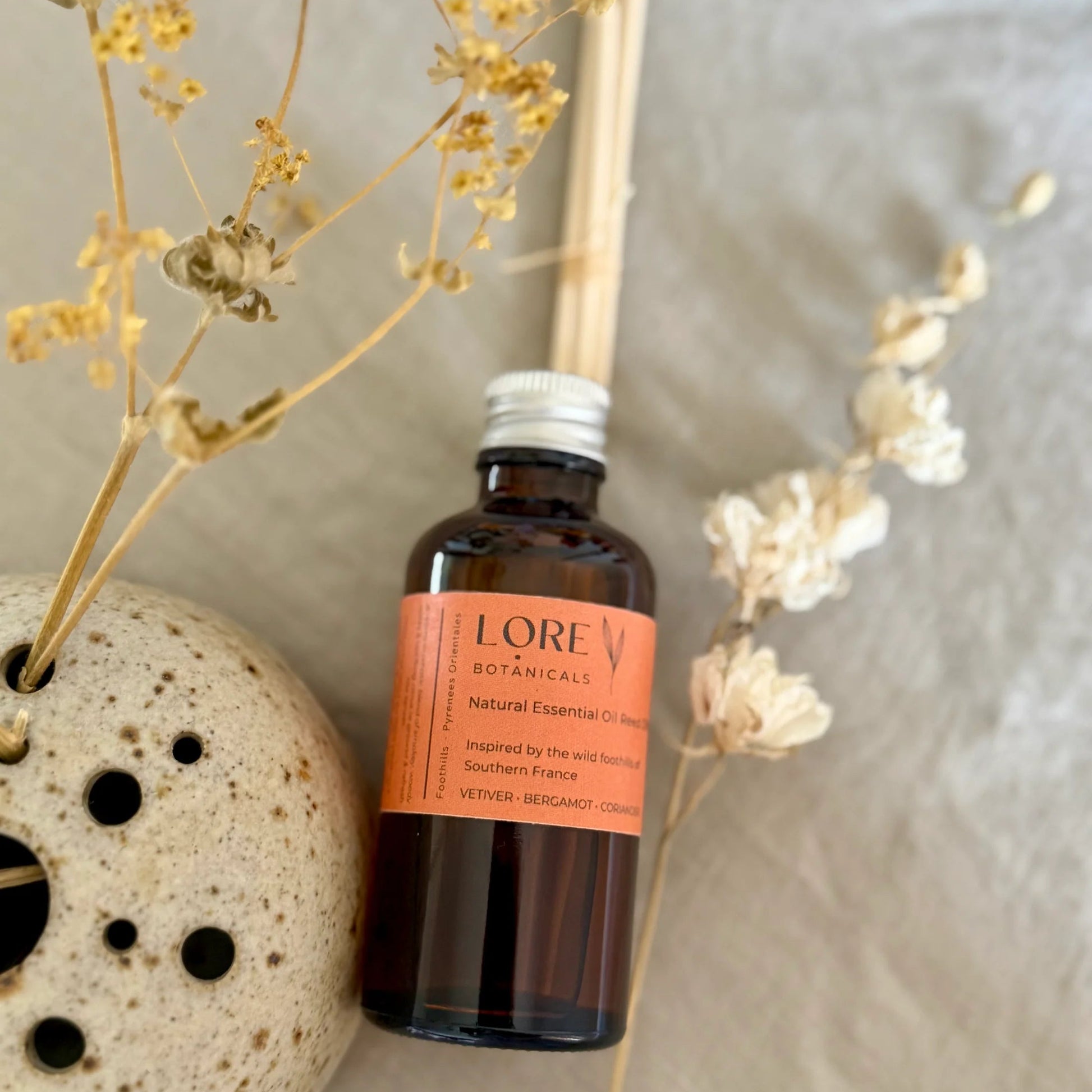 Lore Botanicals bottle with dried flowers and a ceramic holder on a neutral background