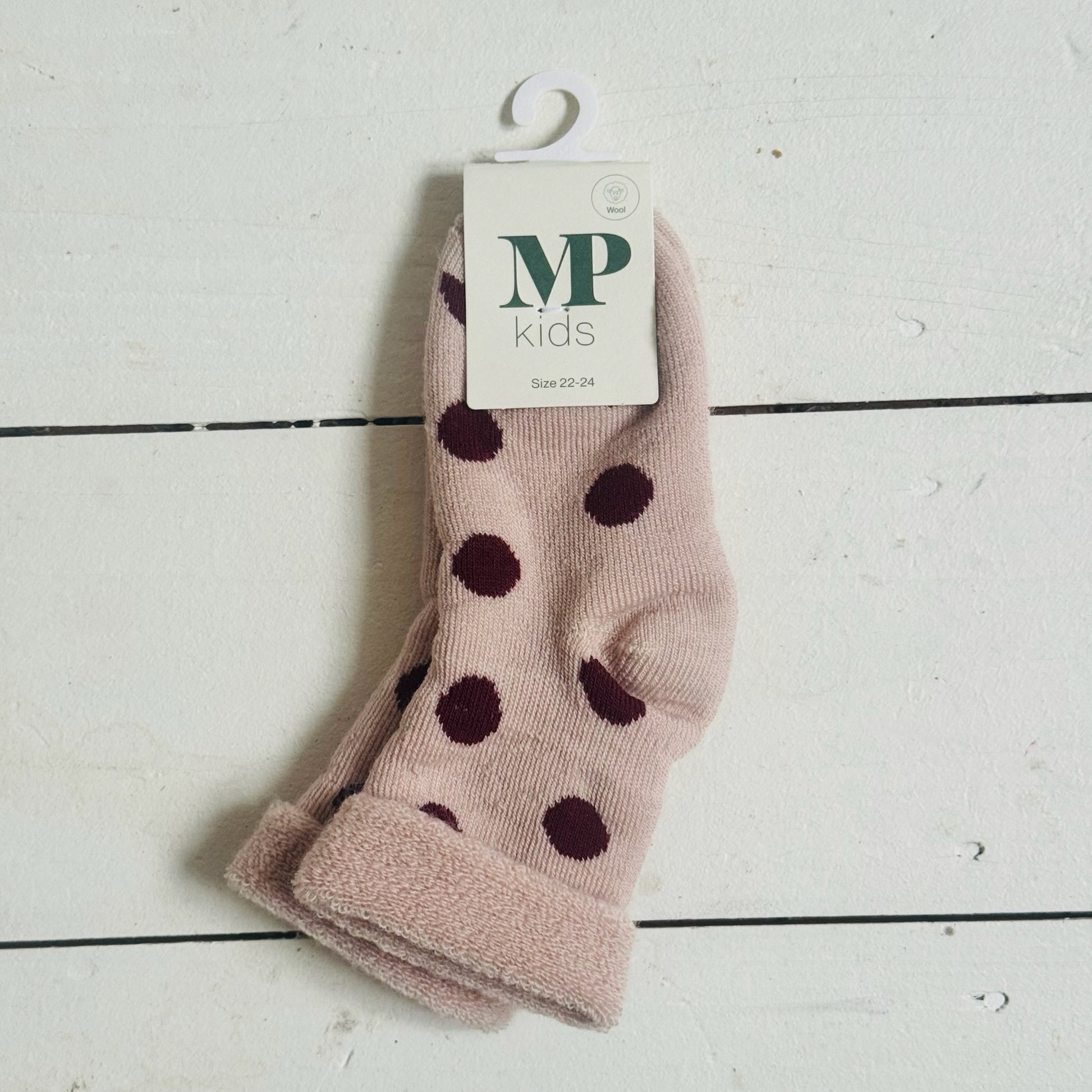 Pink socks with dark polka dots on a white wooden surface, featuring a 'MP kids' label.