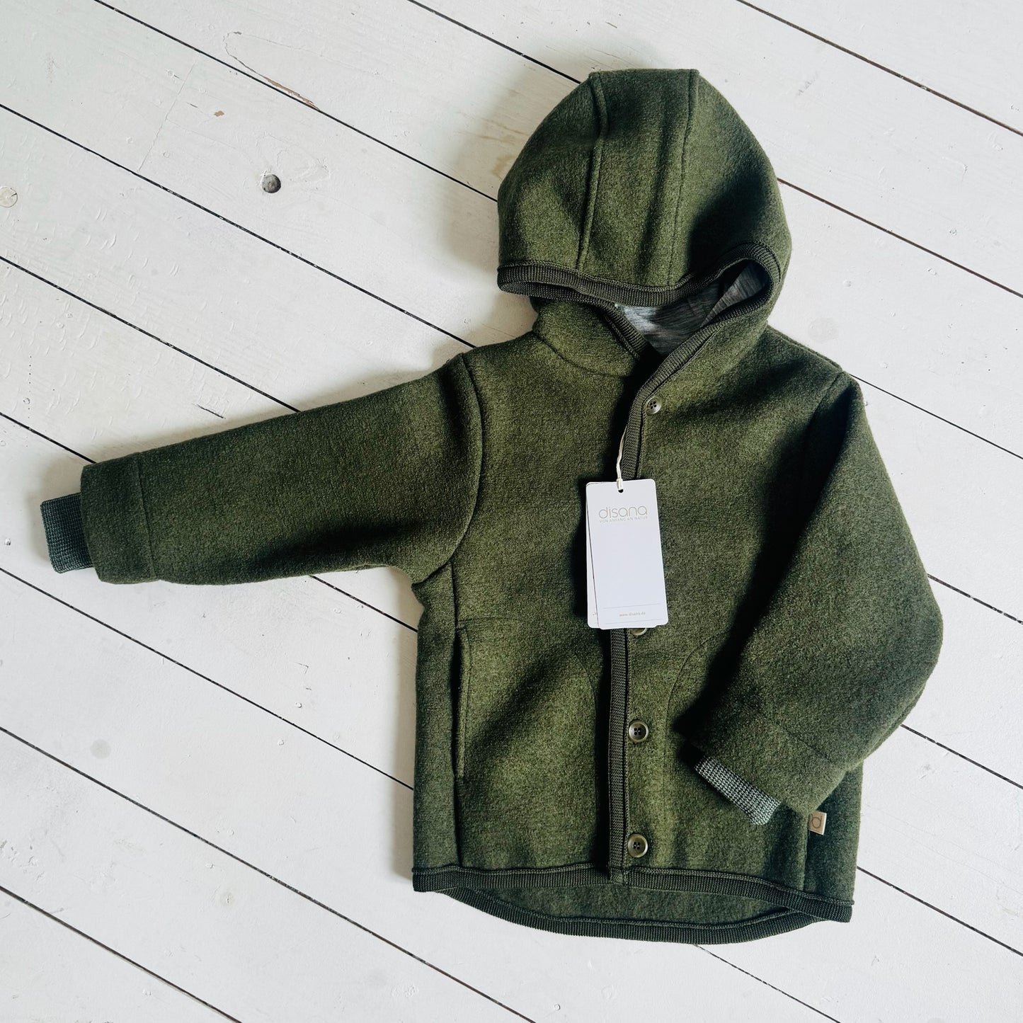 Green children's jacket with a tag on a white wooden floor