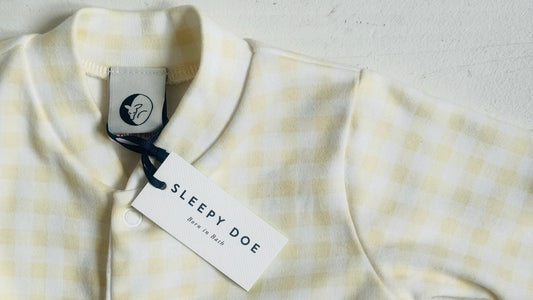 Yellow and white checkered baby outfit with 'Sleepy Doe' tag on a light background