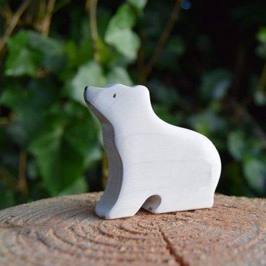 White polar bear figurine on a wooden stump with a green leafy background